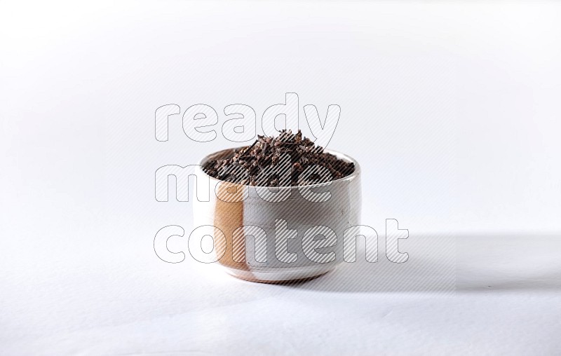 A beige ceramic bowl full of cloves on a white flooring