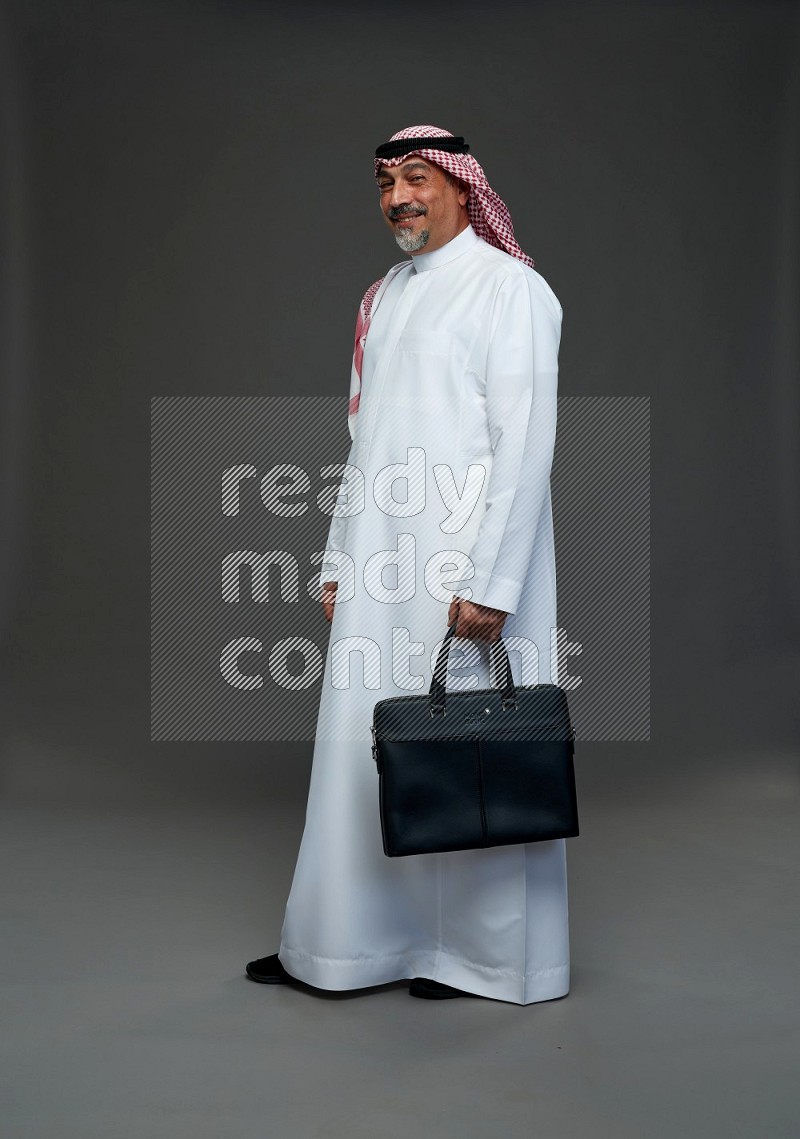 Saudi man with shomag Standing holding bag on gray background