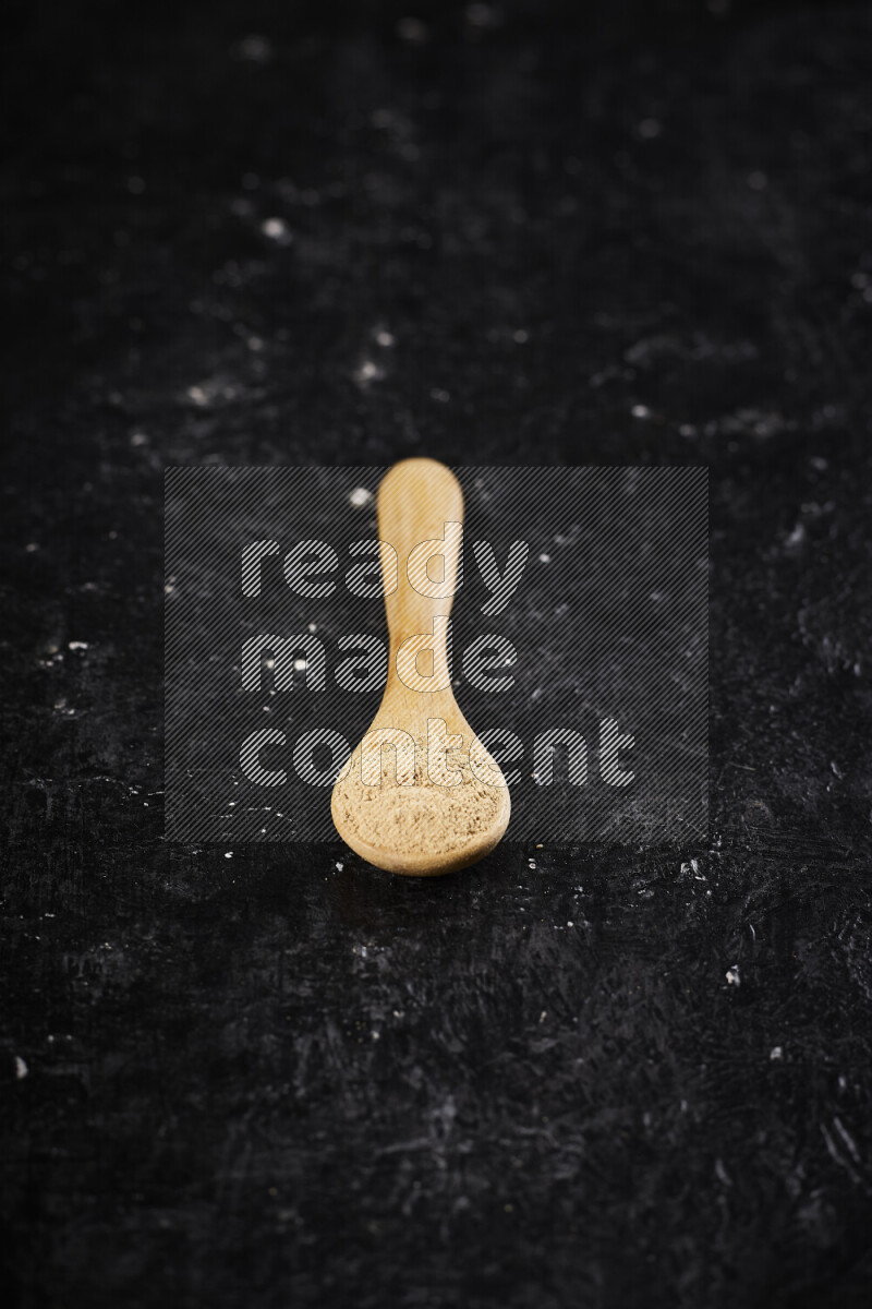 A wooden spoon full of ground ginger powder on black background