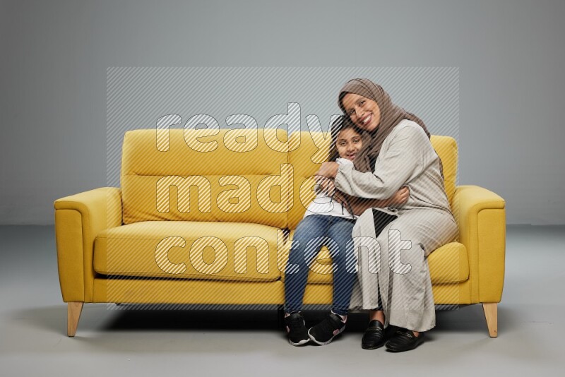 A girl with her mother sitting and interacting with the camera on gray background
