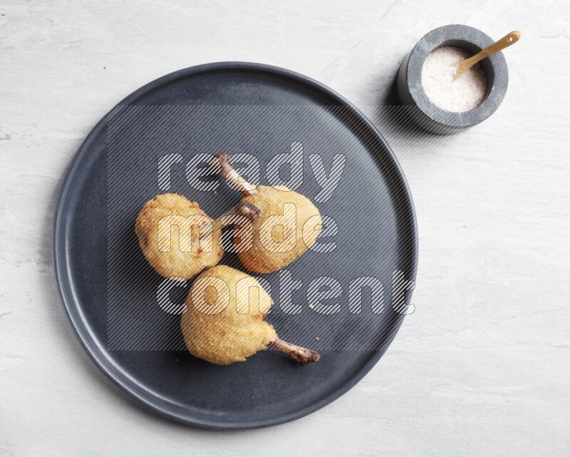 breaded drumstick on round dark grey pottery plate on grey textured countertop