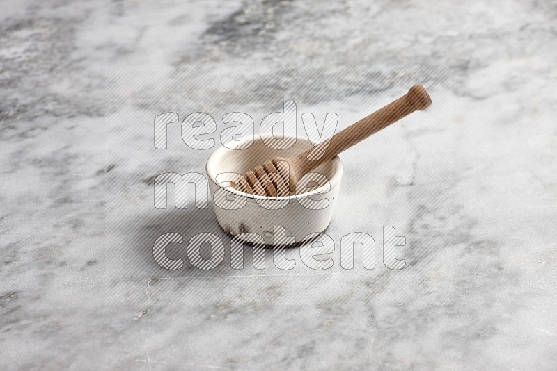 White Pottery Bowl with wooden honey handle in it, on grey marble flooring, 45 degree angle