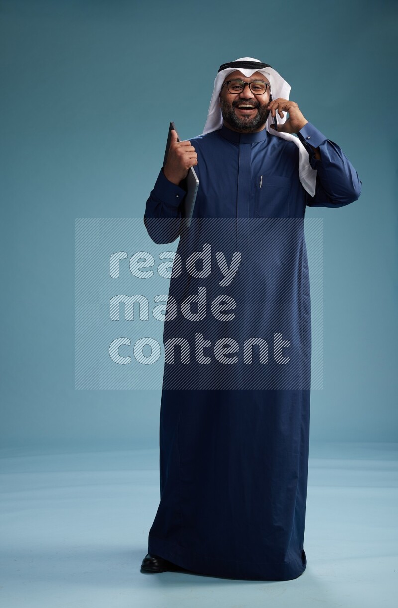 Saudi Man with shimag Standing talking on phone on blue background