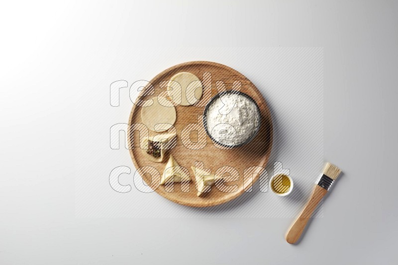 two closed sambosas and one open sambosa filled with meat while flour, and oil with oil brush aside in a wooden dish on a white background