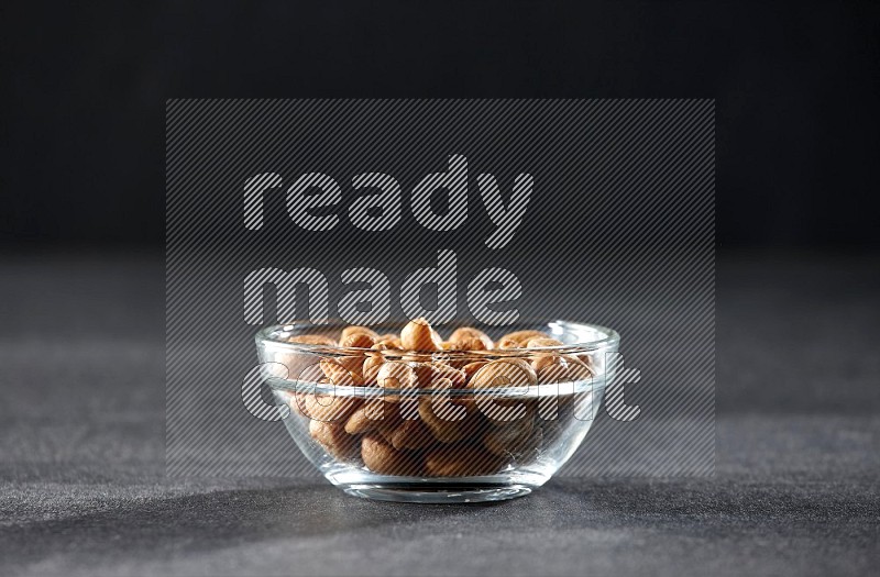 A glass bowl full of cashews on a black background in different angles