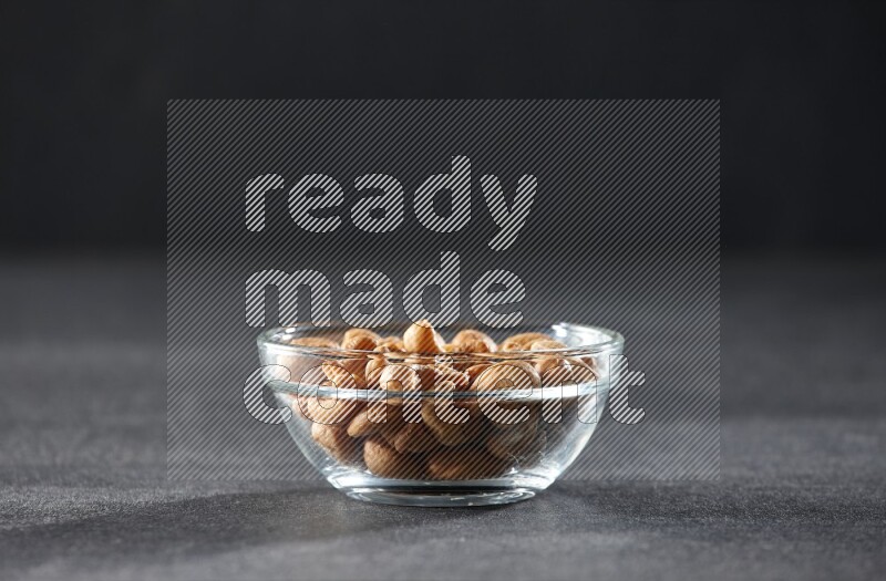 A glass bowl full of cashews on a black background in different angles