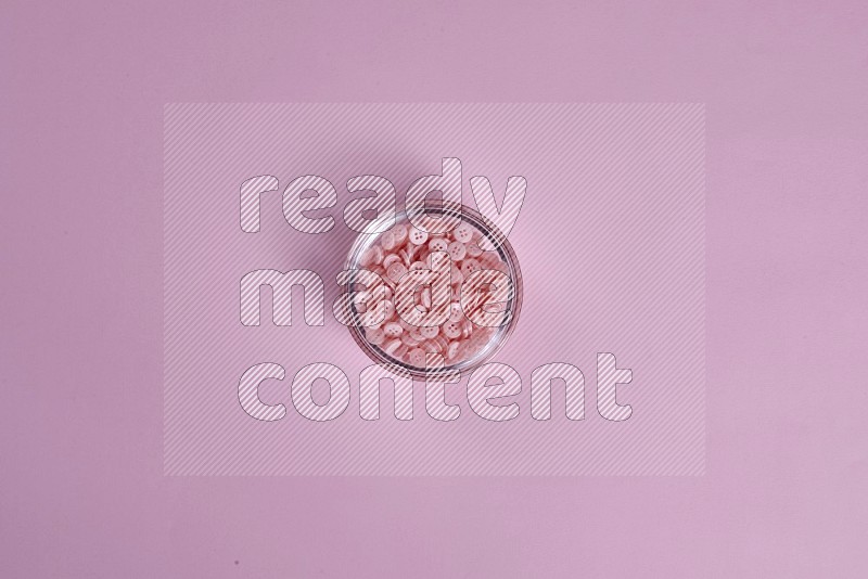 A glass bowl full of pink buttons on pink background