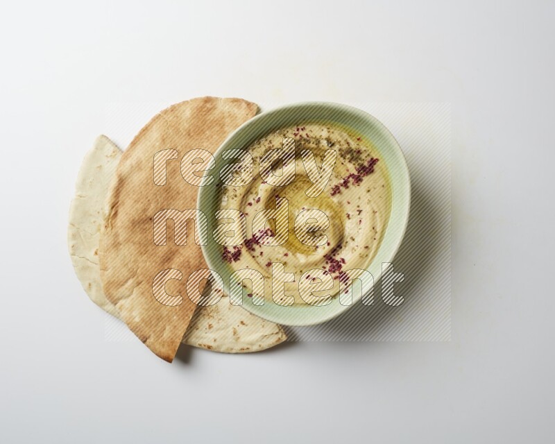 Hummus in a green plate garnished with zattar & sumak on a white background