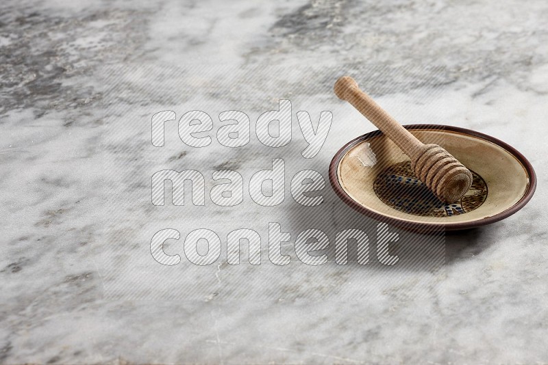 Decorative Pottery Plate with wooden honey handle in it, on grey marble flooring, 45 degree angle