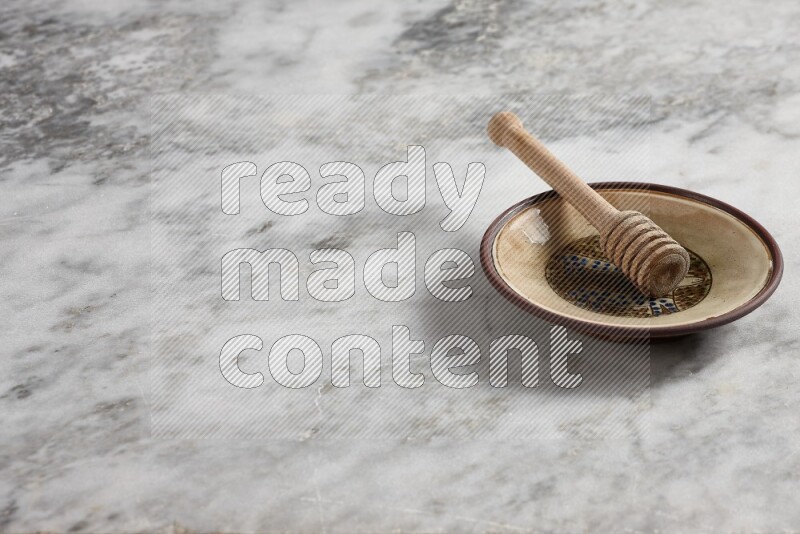 Decorative pottery plate with wooden honey dipper in it on grey marble background