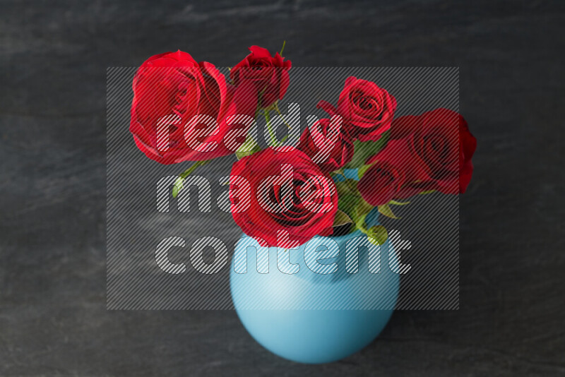 An arrangement of vivid red roses in a blue vase on black marble background