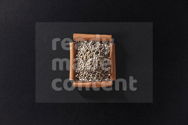 A single square of cinnamon sticks full of white pepper on black flooring