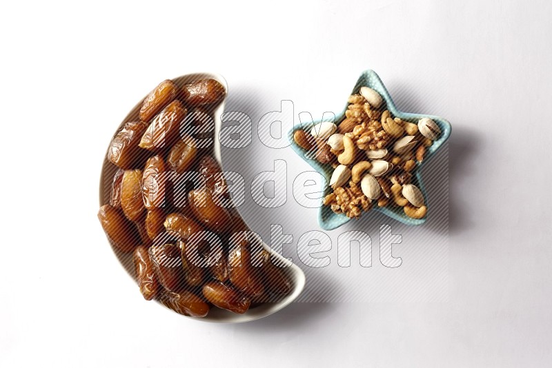 Dates in a crescent pottery plate and a star shaped plate with mixed nuts on white background