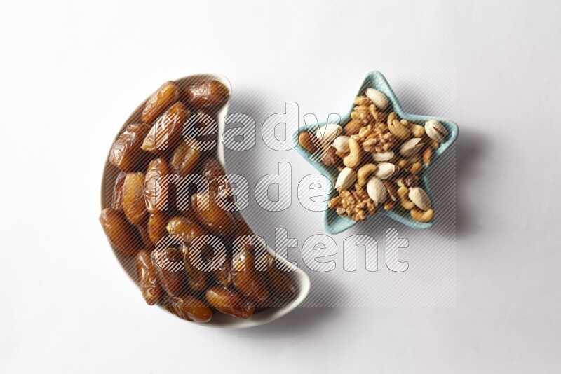 Dates in a crescent pottery plate and a star shaped plate with mixed nuts on white background