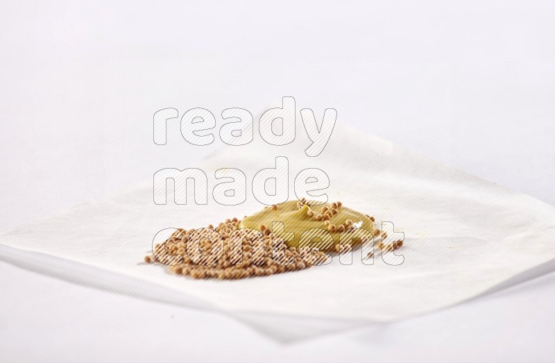 Mustard seeds and mustard paste on a piece of white paper on white flooring