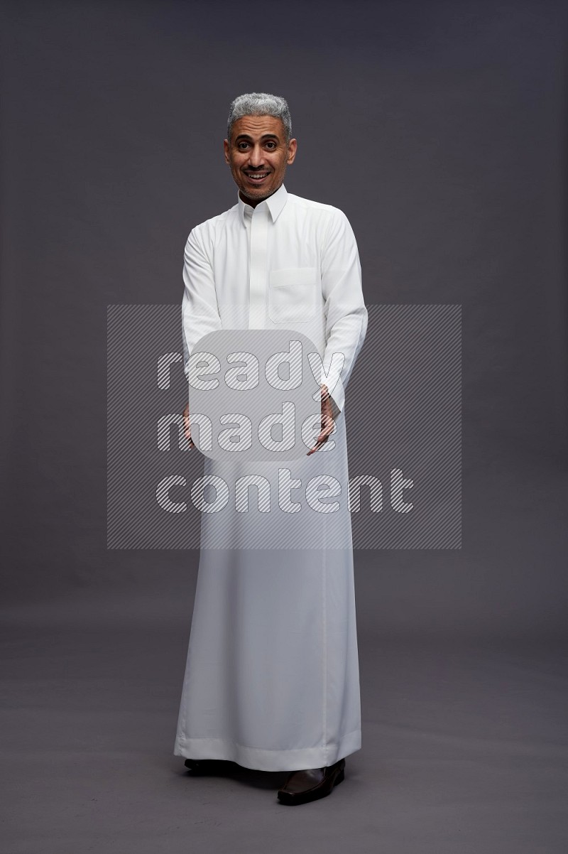 Saudi man wearing thob standing holding social media sign on gray background