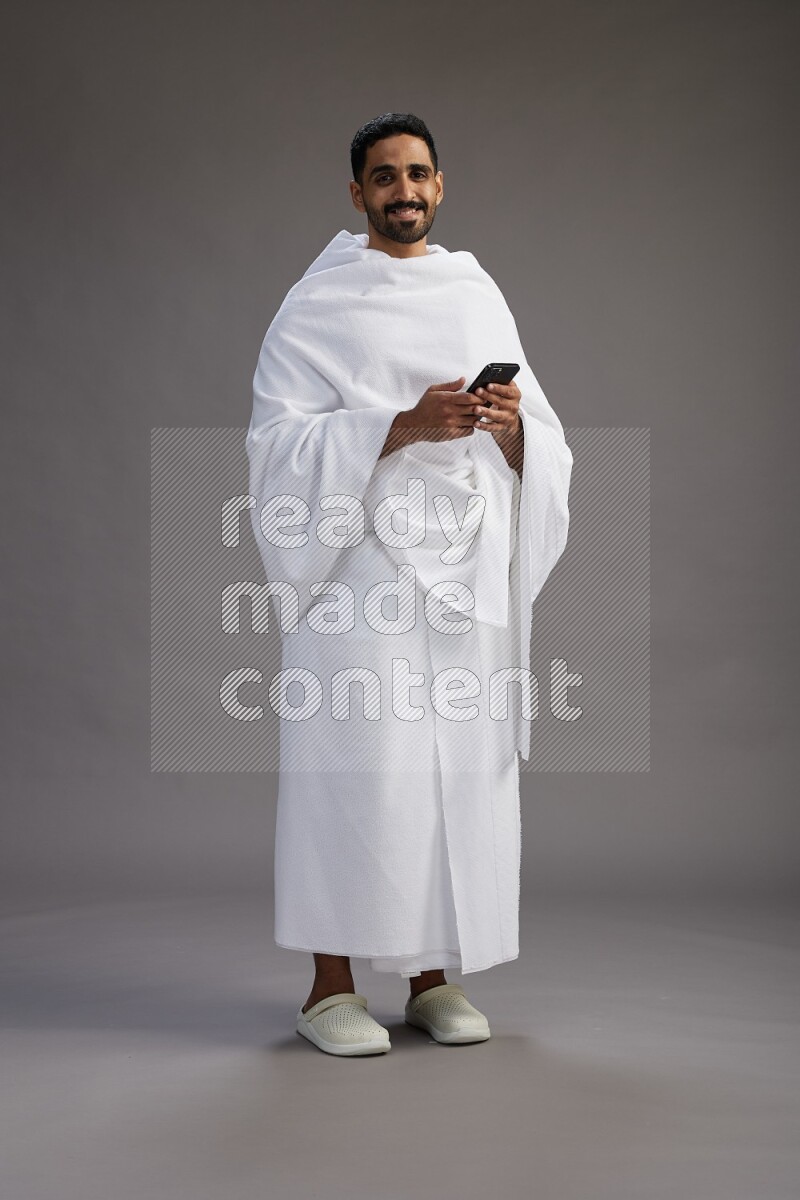A man wearing Ehram Standing texting on phone on gray background