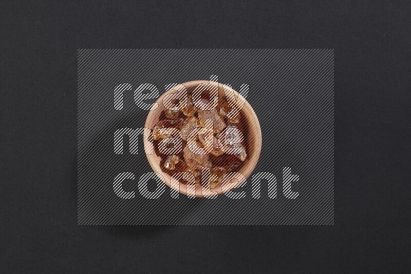 A wooden bowl full of gum arabic on a black flooring