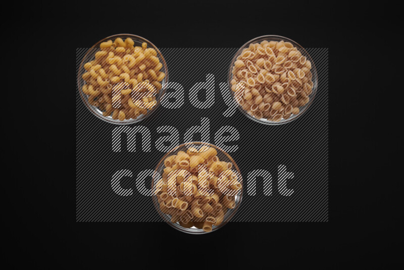 Different pasta types in glass bowls on black background