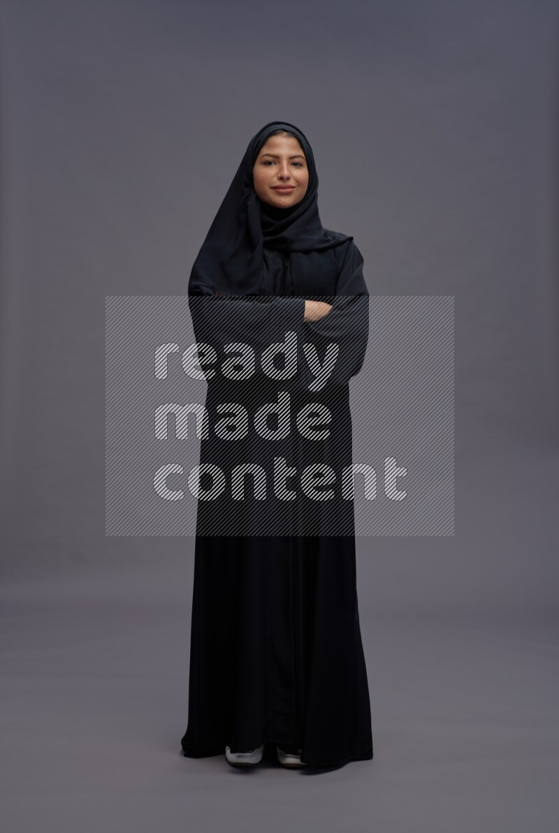 Saudi woman wearing Abaya standing with crossed arms on gray background
