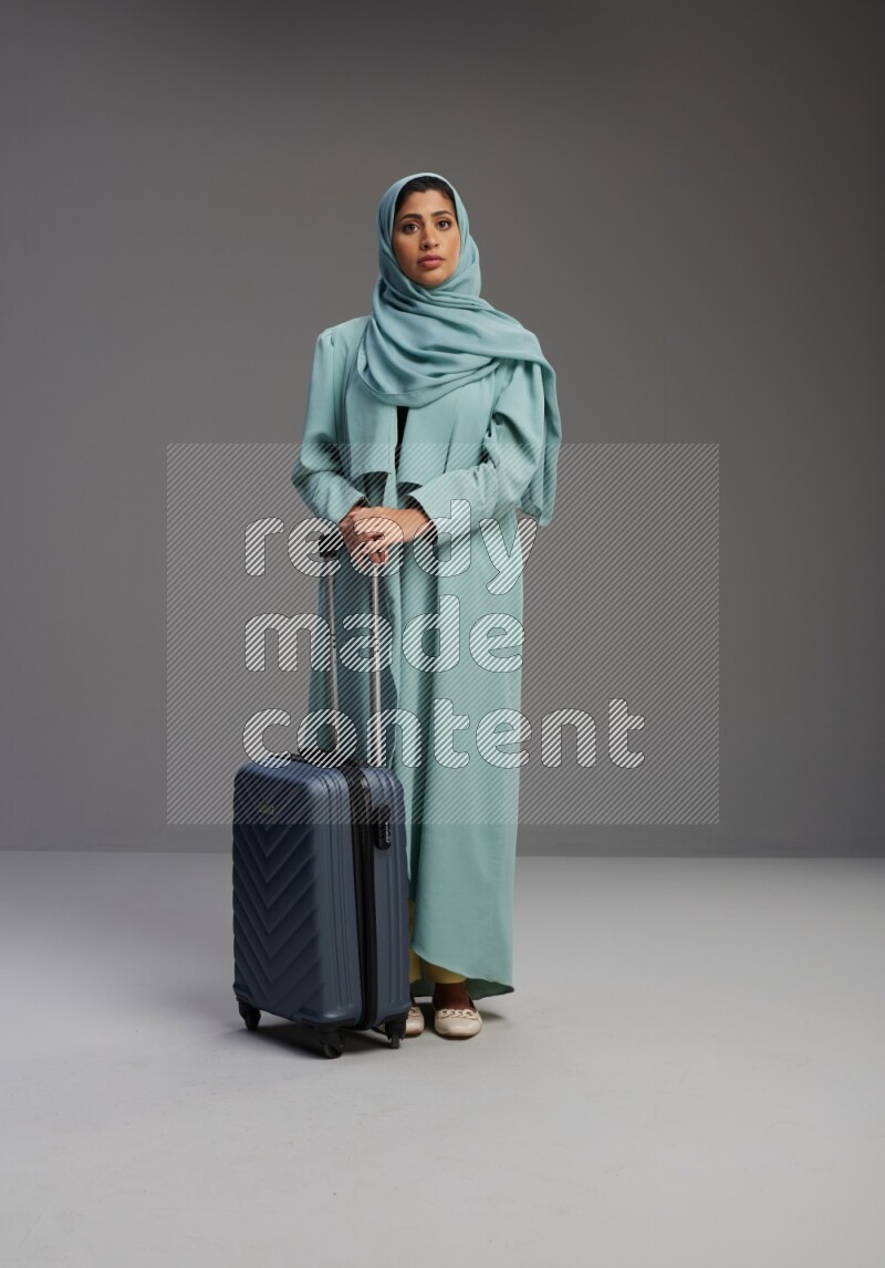 Saudi Woman wearing Abaya standing holding Travel bag on Gray background