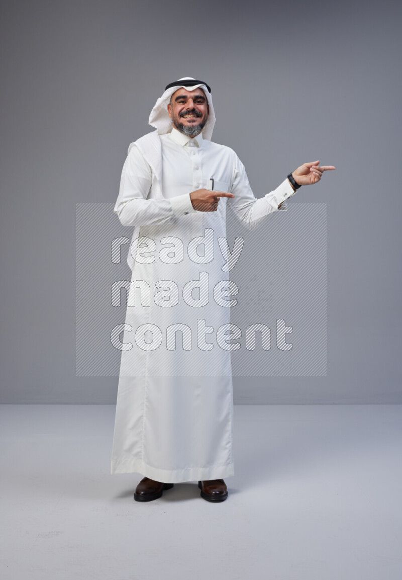 Saudi man Wearing Thob and white Shomag standing interacting with the camera on Gray background