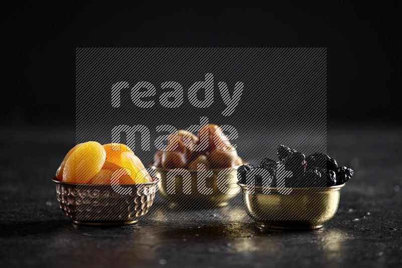 Dried fruits in metal bowls in a dark setup