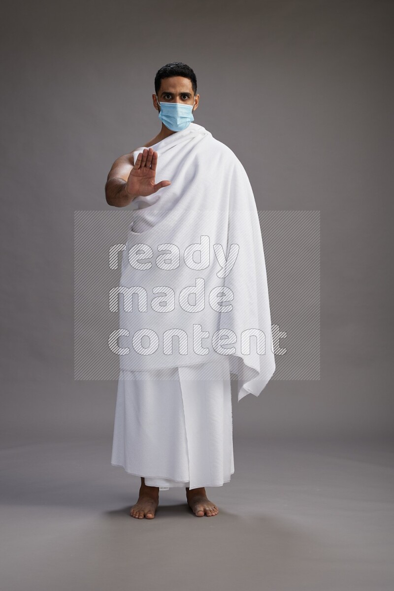 A man wearing Ehram with face mask Standing Interacting with the camera on gray background