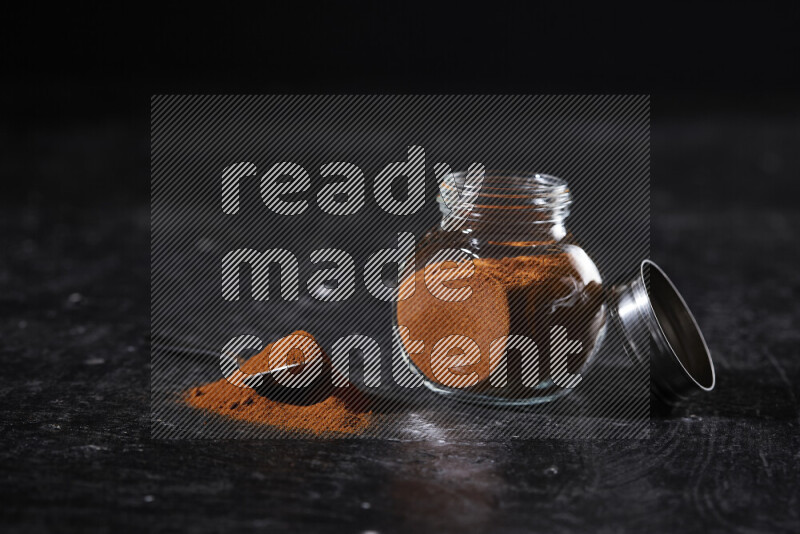 A glass jar full of ground paprika powder on black background