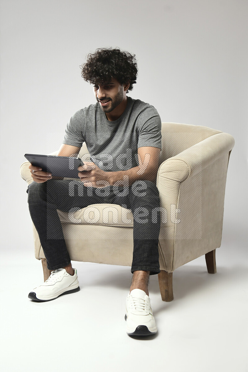 رجل يرتدي ملابس كاجوال يجلس علي كرسي و يلعب علي تابلت علي خلفية بيضاء