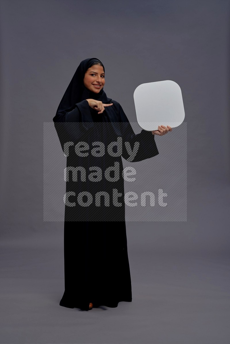Saudi woman wearing Abaya standing holding social media sign on gray background