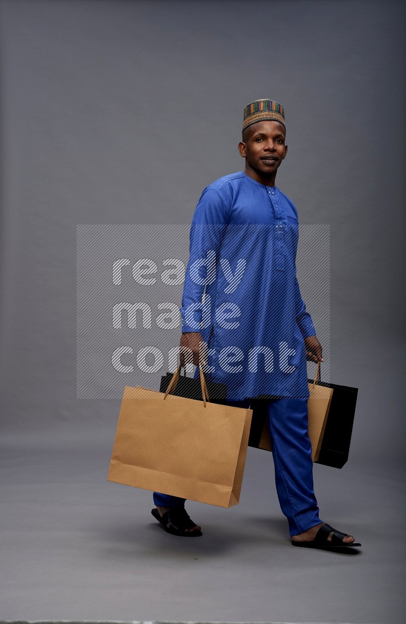 Man wearing Nigerian outfit standing holding shopping bag on gray background