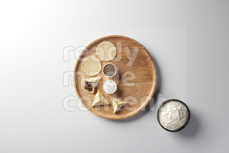 two closed sambosas and one open sambosa filled with meat while flour, salt, and black pepper aside in a wooden dish on a white background
