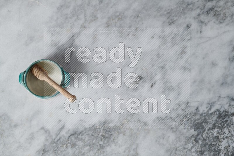 Multicolored pottery bowl with wooden honey dipper in it on grey marble background