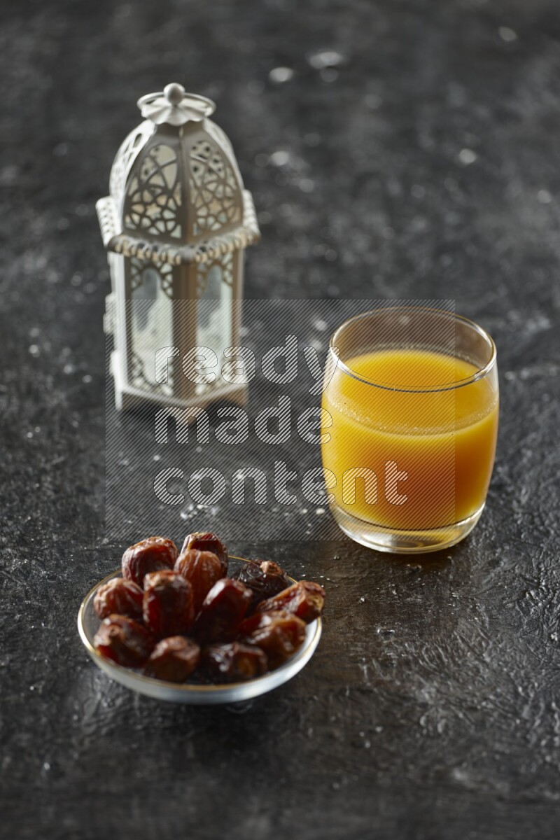 A white lantern with different drinks, dates, nuts, prayer beads and quran on textured black background