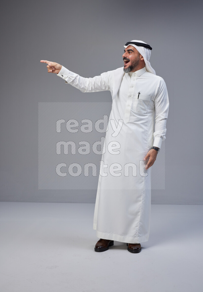 Saudi man Wearing Thob and white Shomag standing interacting with the camera on Gray background