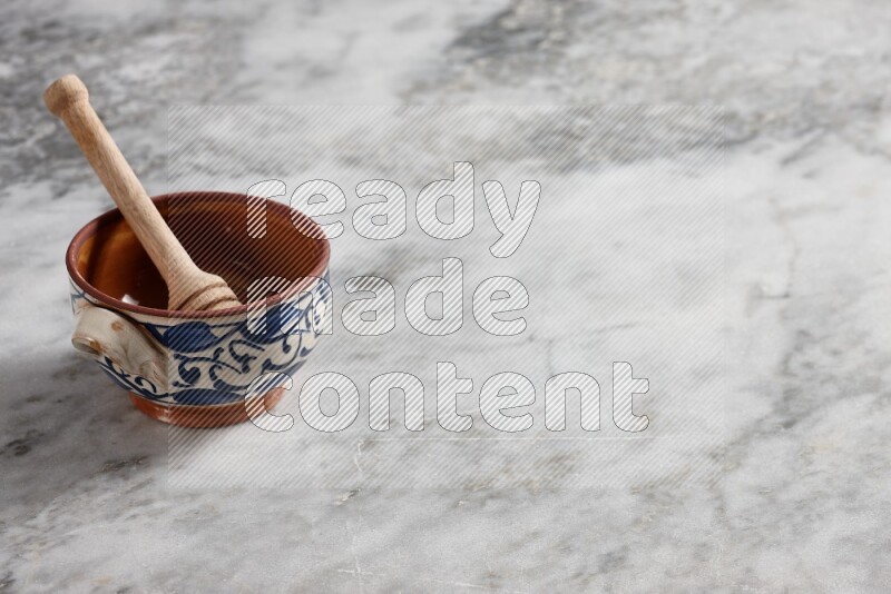 Decorative pottery pot with wooden honey dipper in it on grey marble background