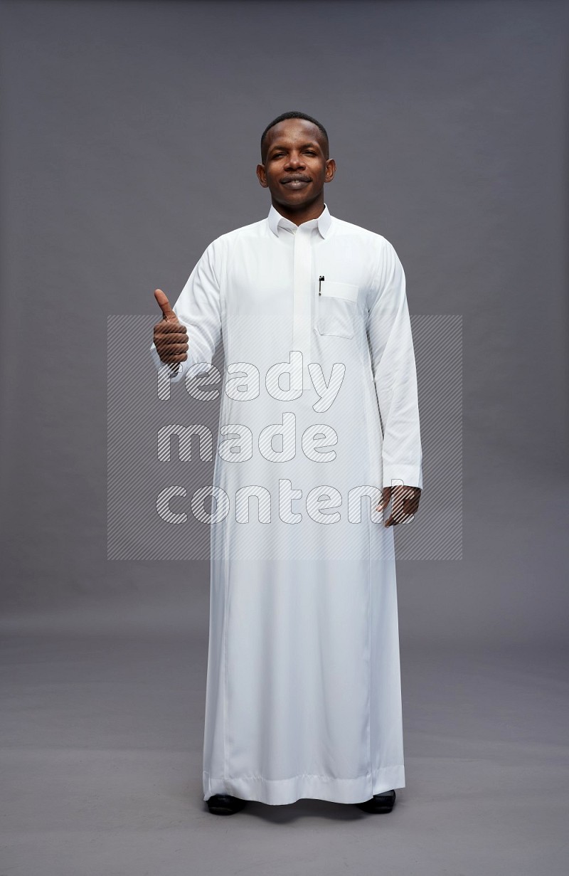 Saudi man wearing thob standing interacting with the camera on gray background