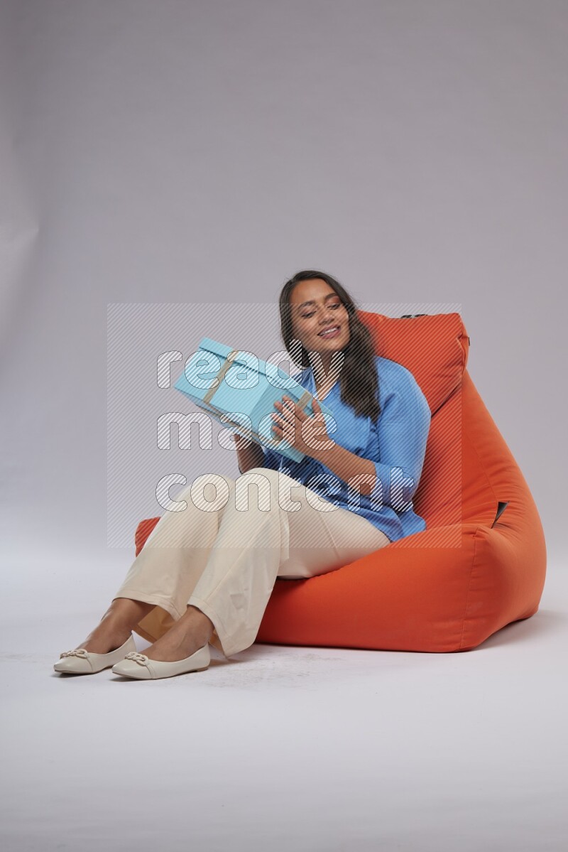 A woman sitting on an orange beanbag and opining a gift
