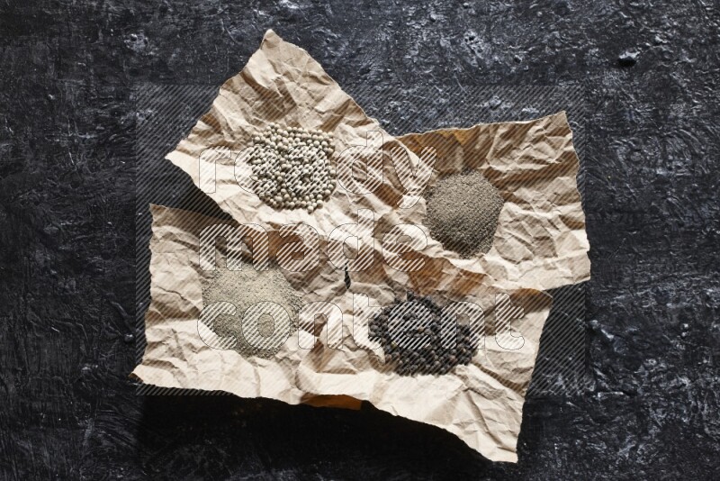 قطع من الورق ممتلئة بحبوب وبودرة الفلفل الأسود والأبيض على أرضية سوداء