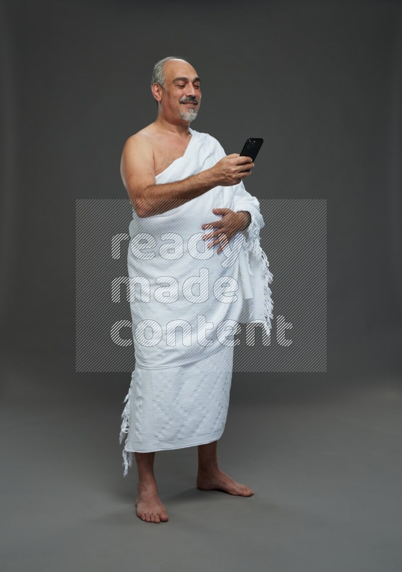 A man wearing Ehram Standing texting on phone on gray background