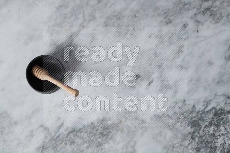 Black pottery bowl with wooden honey dipper in it on grey marble background