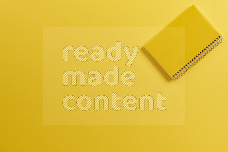 A yellow notebook with different school supplies on yellow background