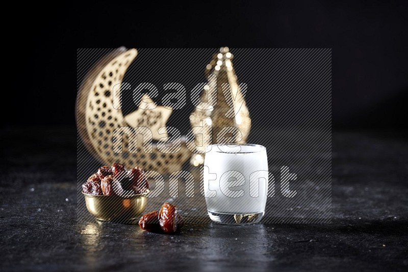 Dates in a metal bowl with sobia beside golden lanterns in a dark setup