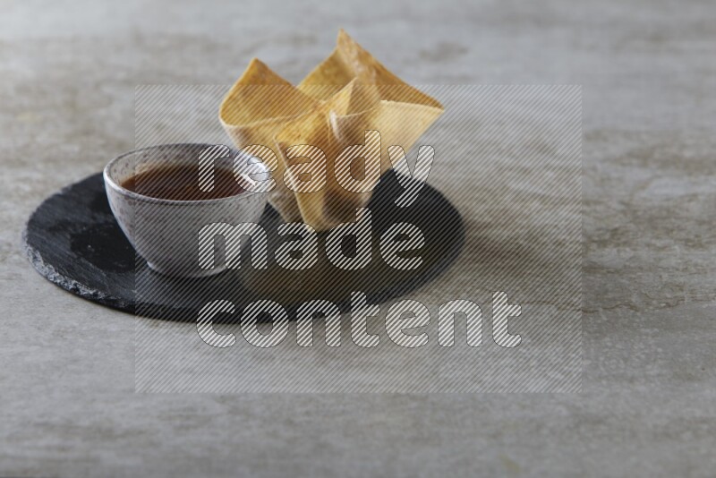 wonton cups with soy sauce ramkin on circle slate on grey textured counter top