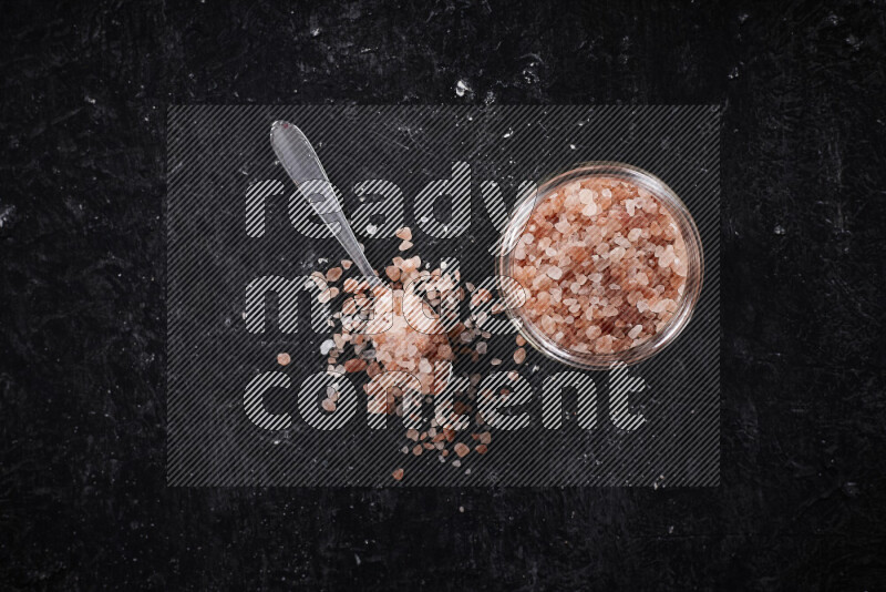 A glass jar full of coarse himalayan salt crystals on black background