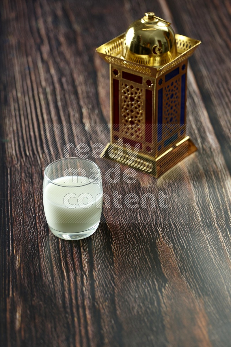 A golden lantern with drinks, dates, nuts, prayer beads and quran on brown wooden background