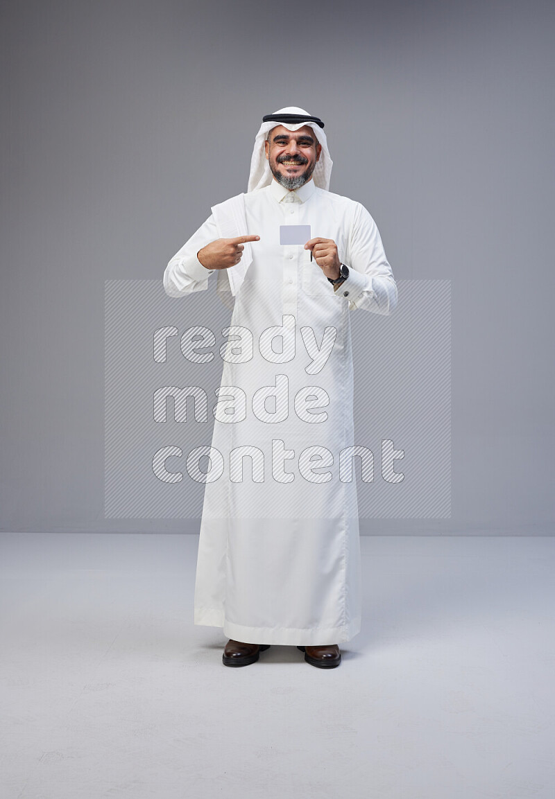 Saudi man Wearing Thob and white Shomag standing holding ATM card on Gray background