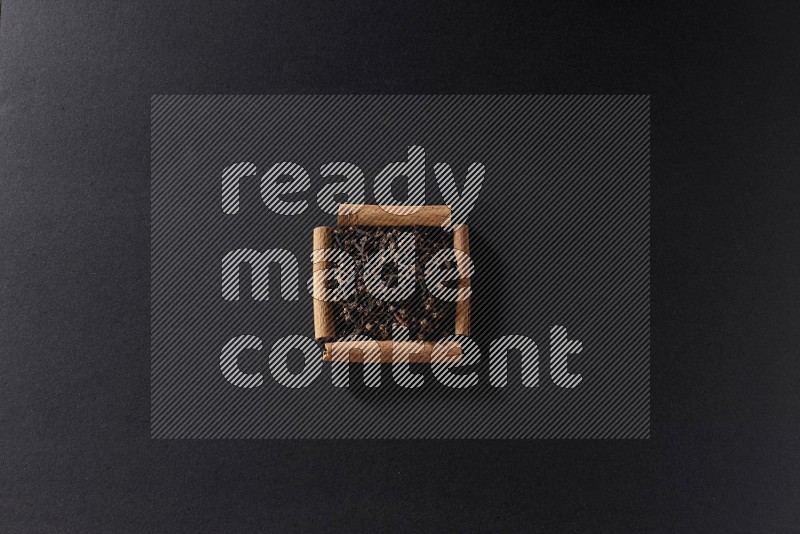 A single square of cinnamon sticks full of cloves on black flooring