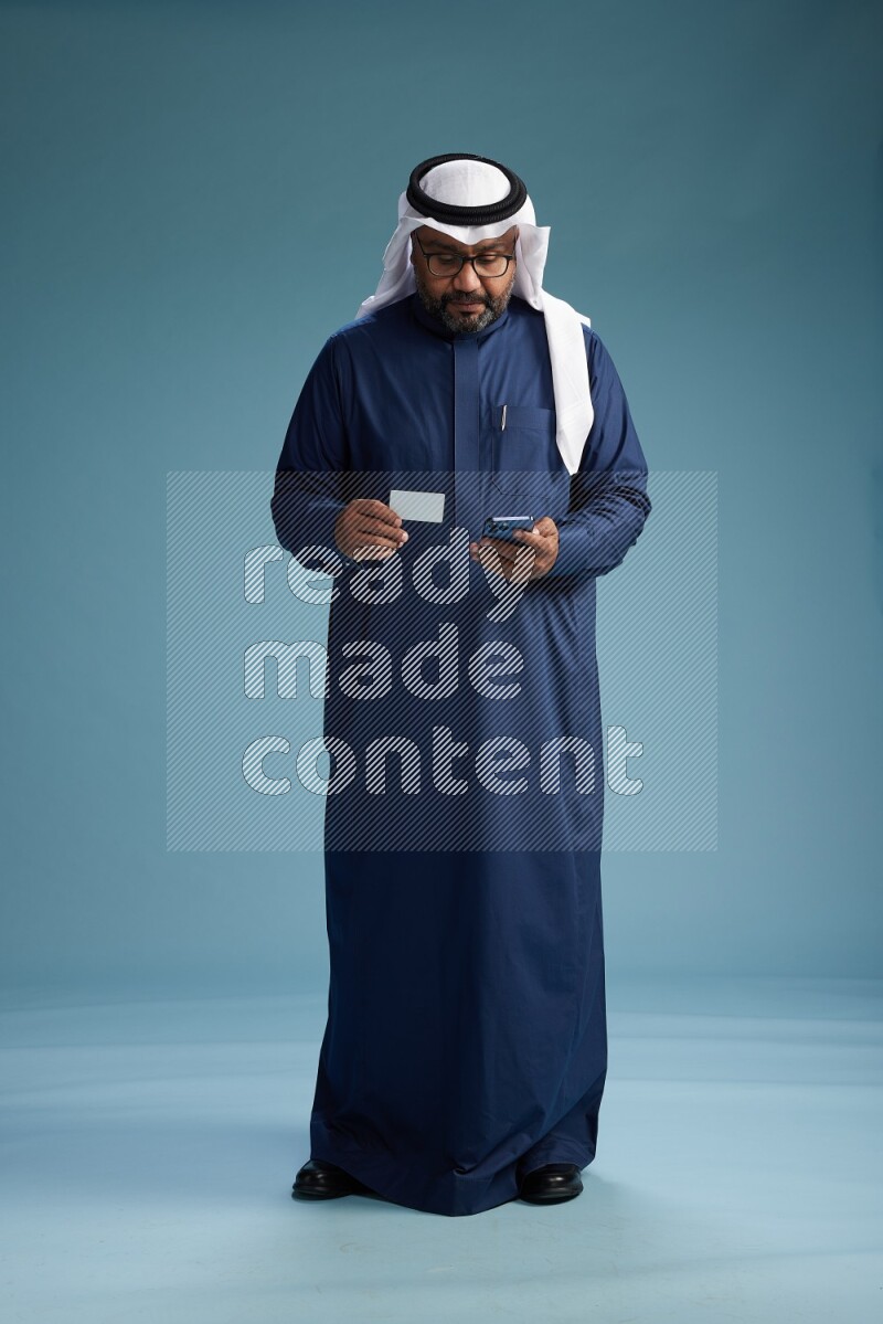 Saudi Man with shimag Standing holding ATM card while talking on phone on blue background